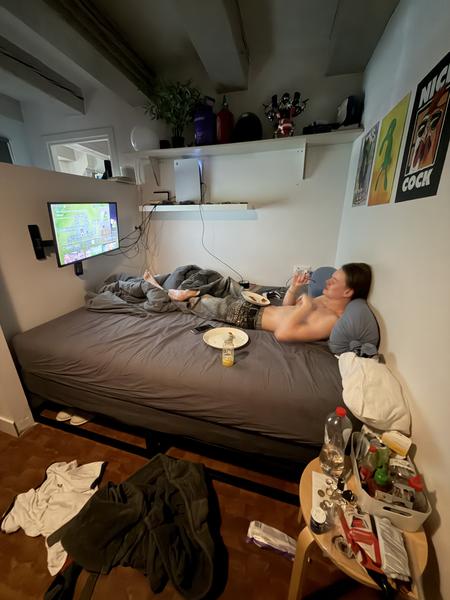 This photo captures a cozy indoor scene at Staalkade, Centrum, Amsterdam, where a person is relaxing on a bed while watching television